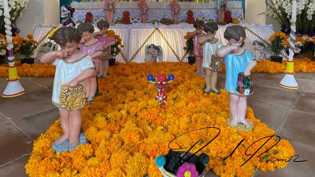 Estatuas de niños llorando sobre tapete de cempasúchil en un altar monumental de Huaquechula, Puebla