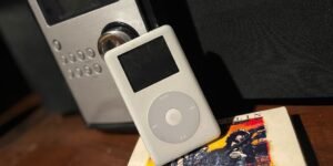 iPod clásico apoyado frente a un minicomponente, sobre un CD de Led Zeppelin, en una mesa de madera.