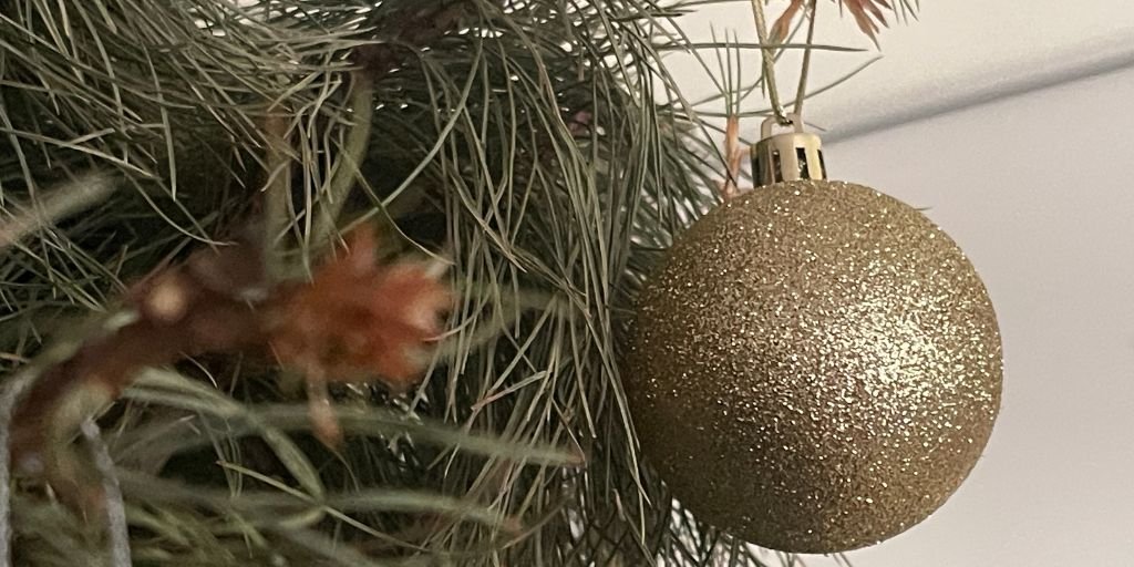 esfera-arbol-navidad Esfera dorada colgada en un árbol de Navidad natural.